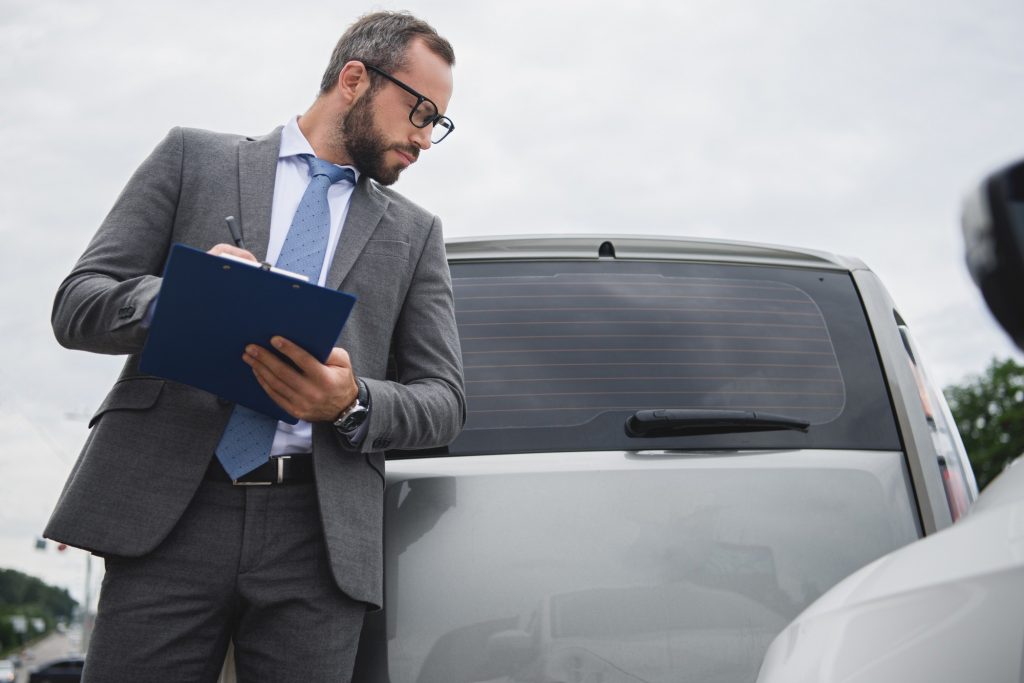 handsome businessman writing something to car insurance after car accident